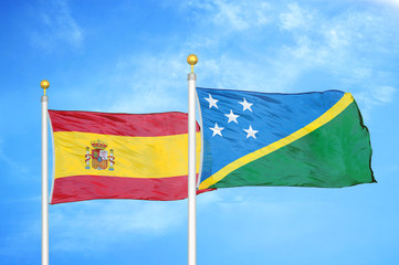 Spain and Solomon Islands two flags on flagpoles and blue cloudy sky