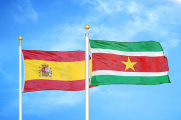 Spain and Suriname two flags on flagpoles and blue cloudy sky