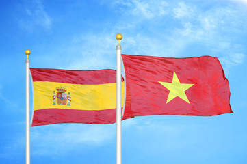 Spain and Vietnam two flags on flagpoles and blue cloudy sky