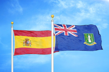 Spain and Virgin Islands British two flags on flagpoles and blue cloudy sky