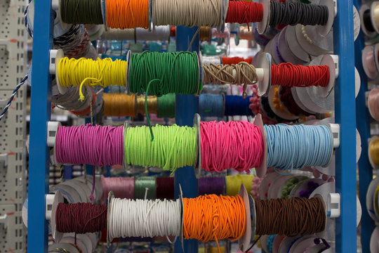 multi-colored braids and elastic bands wound on bobbins on the counter of the store for needlework, sewing and creativity