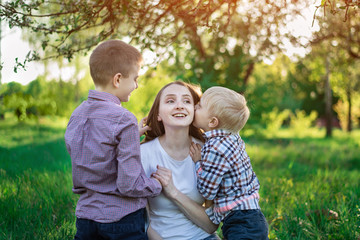 Fototapeta premium Mom with two sons in the Park. Child is kissing his mother. Happy motherhood