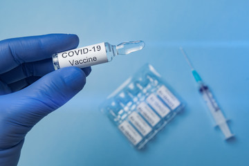 Naklejka premium Ampoule with the vaccine COVID-19 in the hand in a medical glove. Close-up. Syringe on the background.