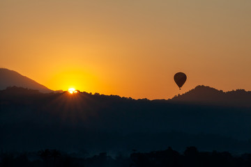 The rising sun in the morning and hot air ballon fly ovre mountain with Amazing yellow and orange color