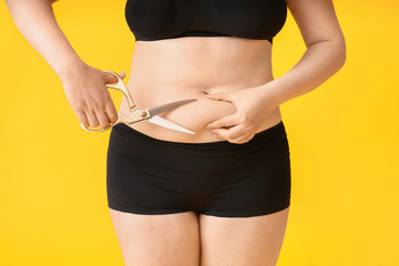 Overweight woman with scissors on color background. Weight loss concept