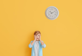 Surprised little boy near color wall with clock