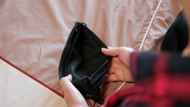 brunette in checkered shirt opens empty black wallet and throws various coins on bed close backside upper view