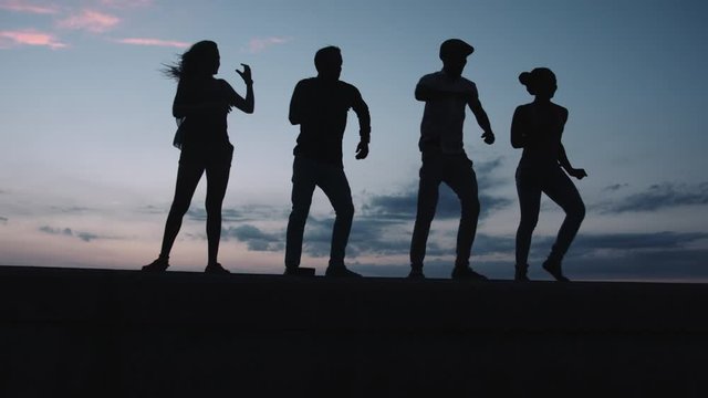 Men and women dancing and having fun on retaining wall at sunset