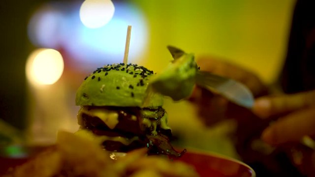 Healthy raw avocado burger, sesame seeds and fresh vegetable served on a plate is being cut by knife. 