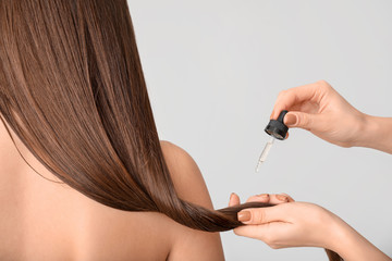Applying of cosmetics on woman's hair against grey background