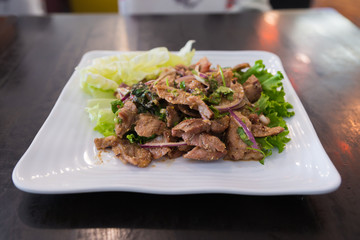 Thai style spicy grilled pork neck salad with red onion in white plate called as 