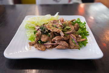 Thai style spicy grilled pork neck salad with red onion in white plate called as "Nam Tok Moo"