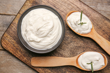 Bowl and spoons with tasty sour cream on wooden table