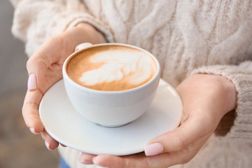 Woman with cup of tasty cappuccino outdoors, closeup