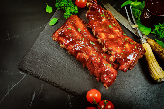 Pork ribs with barbecue sauce on black stone board. Top view.
