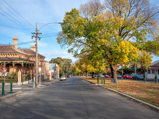 Fototapeta na wymiar Quiet neighborhood street lined with old residential houses and autumn trees. Typical suburban view with Australian homes in one of Melbourne's inner suburbs. North Melbourne, VIC Australia