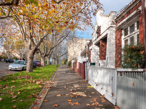 The pedestrian sidewalk along with Victorian style residential houses in a quiet neighborhood street in one of Melbourne's inner suburbs. North Melbourne, VIC Australia. - Powered by Adobe