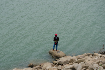 Fototapeta na wymiar Fishing man on the rock beside the water in the lake