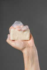 Caucasian male hand holding plain bar of soap with lather and bubbles