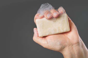 Caucasian male hand holding plain bar of soap with lather and bubbles