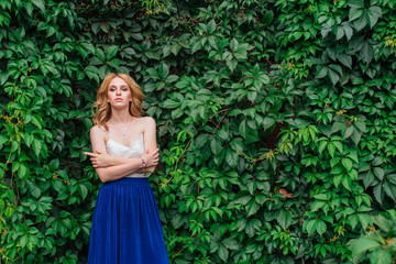 Portrait of a young beautiful woman, standing next to the wall of wild grape leaves.