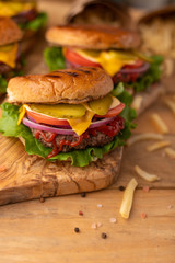 Cooked on the grill burger on a wooden table. Restaurant menu. Cheeseburger with beef, cheese, onions, tomatoes, cucumbers and french fries. Tasty fast food. Street junk food.