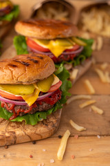 Cooked by a chef burger on a wooden table. Restaurant menu. Cheeseburger with beef, cheese, onions, tomatoes, cucumbers and french fries. Tasty fast food. Junk and fat food.