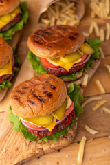 Cooked on the grill burger on a wooden table. Restaurant menu. Cheeseburger with beef, cheese, onions, tomatoes, cucumbers and french fries. Tasty fast food.