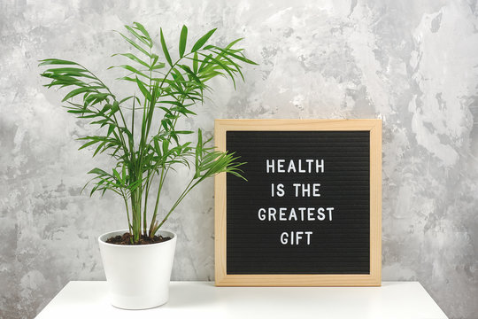 Health is the greatest gift. Motivational quote on letter board on white table and green exotic palm flower in pot, gray stone wall. Concept Health Care and Medicine, inspirational quote of the day