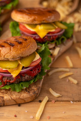 Grilled burger on a wood table with salt and pepper. Homemade tasty cheeseburger on the cutting board with beef, cheese, onions, tomatoes, cucumbers, sauce and french fries. Fast food concept