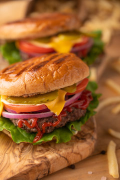 Grilled hot cheeseburger on a wood cutting board. Homemade burger with beef, cheese, vegetables, crispy buns and salt fries on a rustic table. Restaurant menu. Vertical picture, front view, close up