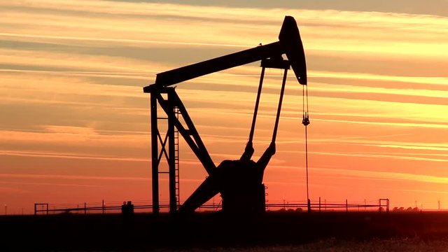 Silhouetted pumpjack in the oil field at sunset