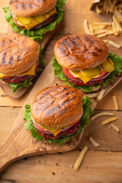 Fresh hot burger with french fries. Meal on a cutting kitchen board on a wooden table. Cheeseburger with meat, cheese, tomatoes, cucumbers and onions. Street junk food. Vertical picture, top view