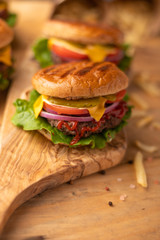 Fresh hot juicy burger with salty french fries. Meal on a cutting kitchen board on a wooden table. Cheeseburger with meat, cheese and vegetables. Vertical picture. American cuisine. Rustic style