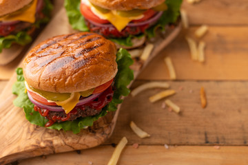 Fresh hot juicy burger with salty french fries. Meal on a cutting kitchen board on a wooden table. Tasty cheeseburger with beef, cheese and vegetables. American cuisine. Cooking junk food concept