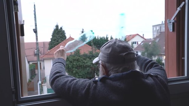 Old man clap at eight pm with plastic bottles at window during virus containment