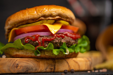 Tasty beef burger, french fries and sweet soda drink on a wooden board on a black background. Cheeseburger cooked with cheese, meat, vegetables and crispy buns. American cuisine. Close up, front view