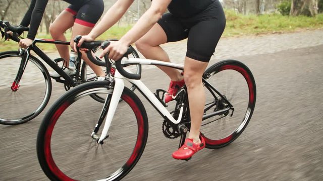 Cropped shot of women cycling in park. Partial view of athletic sportswomen in sportswear cycling on bikes during competition, tracking shot. Cycling concept