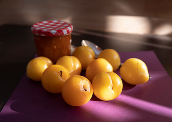 Close-up of yellow plums and a jam jar on a wooden and purple background