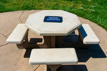 Concrete picnic table in public park with Surface Not Disinfected sign