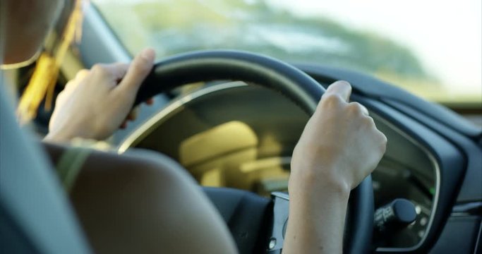 Woman driving car at sunset with hands at 10 and 2 on the steering wheel - close up