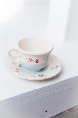Vintage tea-ware pale blue color on white table. Tea pot and cup with painted roses