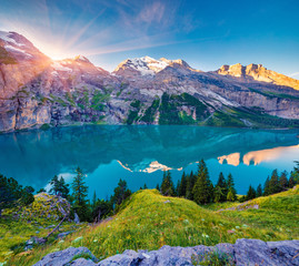 First sunlight gloving mountain hills and meadows. Picturesque summer view of unique Oeschinensee...
