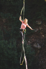A woman is walking along a stretched sling over a forest, Purposeful girl goes to the goal.