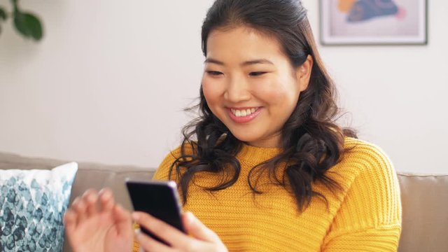 technology, people and internet concept - happy smiling asian woman with smartphone having video call at home