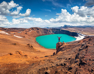 Tourist standing on the edge of cliff on Krafla Viti Crater lake with raised hands and enjoying...