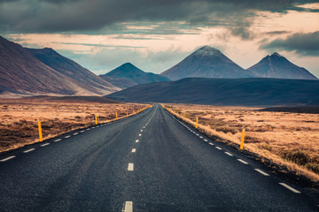 Empty asphalt road with dramatic cloudy sky. Typical icelandic landscape with volcanic hills. Image of travel concept background.