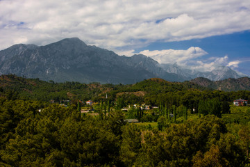 Mountains, many green trees, clouds on a blue sky