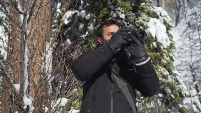 young traveller capturing photos of Yosemite waterfall using his professional camera at winter with thick snow
