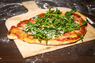 Pizza auf Holzschieber frisch aus dem Ofen, auf Küchentisch mit Mehrresten, mit Rucola und...
